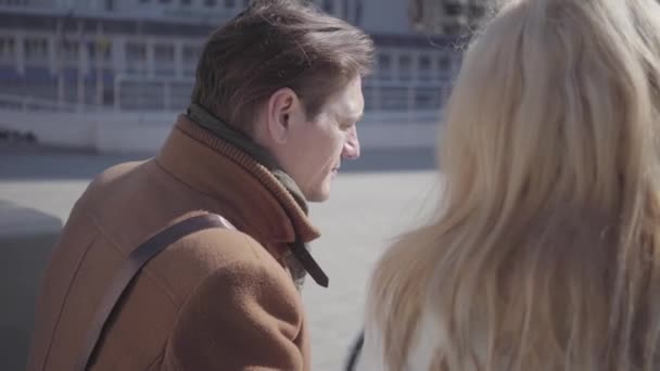 Portrait of handsome man and pretty blond woman in warm jacket sitting at the city street talking. The couple chatting discussing enjoying being together. - Materiał filmowy, wideo