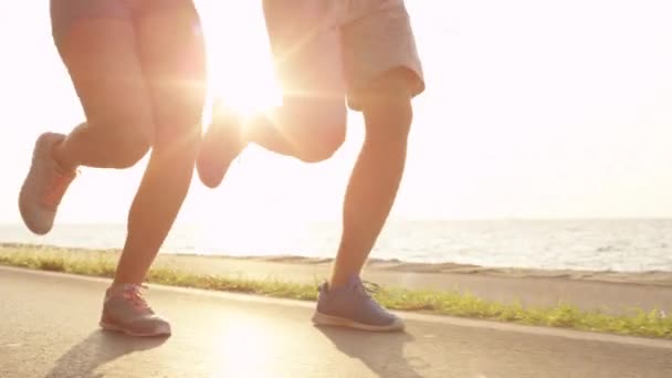 Genç erkek arkadaşı ve kız arkadaşı birlikte güneşli sahilde jogging. Huzurlu okyanus boyunca sportif Tarih jog üzerinde kadın aktif adam. Yaz aylarında açık havada egzersiz mutlu çift. - Video, Çekim