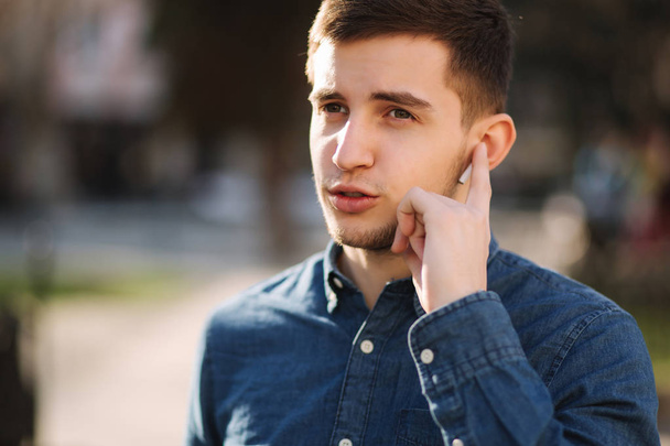 El hombre guapo pone su dedo en los auriculares inalámbricos y habla. Retrato del hombre hace conversación por teléfono
 - Foto, Imagen