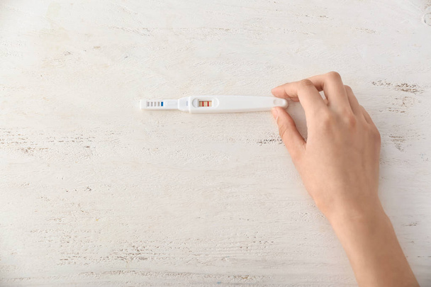 Mano femminile con test di gravidanza su sfondo bianco in legno
 - Foto, immagini