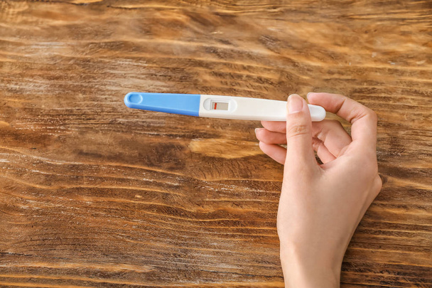 Vrouwelijke hand met zwangerschapstest op houten achtergrond - Foto, afbeelding