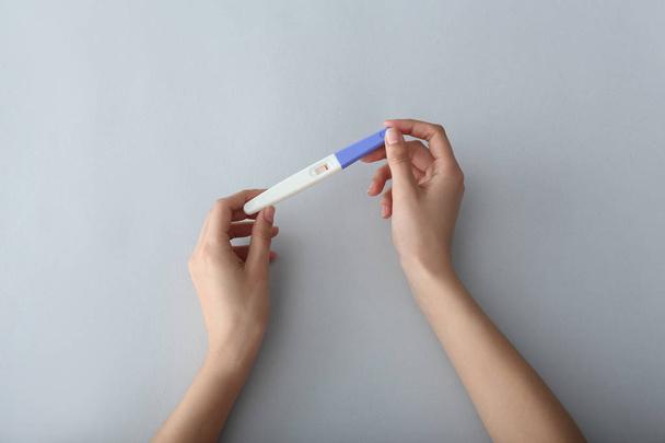Γυναικεία χέρια με τεστ εγκυμοσύνης σε ανοιχτόχρωμο φόντο - Φωτογραφία, εικόνα