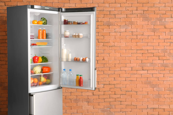 Відкритий холодильник повний їжі біля цегляної стіни
 - Фото, зображення