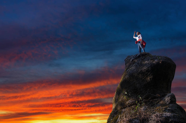 Mulher em pé no pico da montanha rochosa ao pôr do sol
 - Foto, Imagem