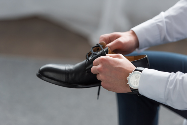 cropped view of man with watch on hand holding black shoe  - Fotó, kép