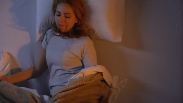 Όμορφη κοπέλα που κείτεται στο ορθοπεδικό κρεβάτι της, απενεργοποιώντας το φως και κοιμισμένη - Πλάνα, βίντεο