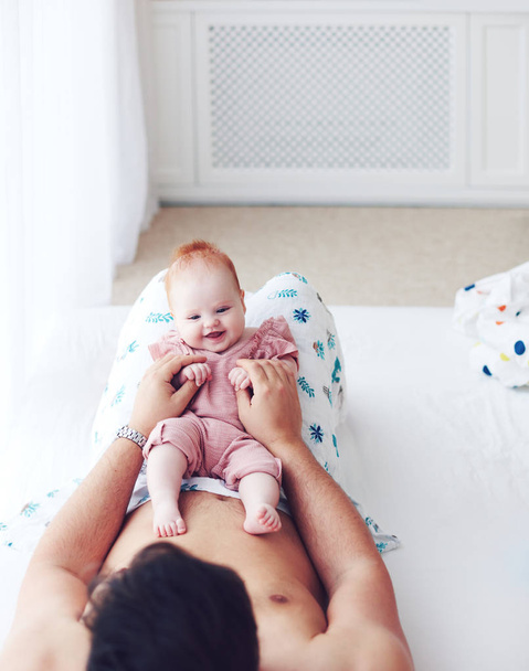jovem pai brincando com bonito bebê bebê filha na cama, em casa
 - Foto, Imagem