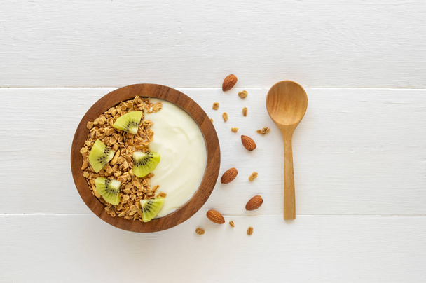 Vue de dessus du yaourt dans un bol en bois avec granola, kiwi frais, menthe, amande et cuillère sur table en bois bleu. Concept d'aliments santé
. - Photo, image