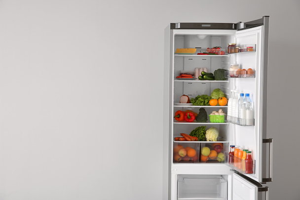 Відкритий холодильник повний їжі біля білої стіни
 - Фото, зображення