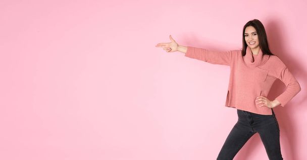 Pretty young girl full of energy posing in pink sweater on pink background - Photo, Image