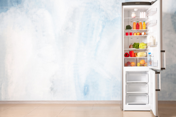 Nyitott hűtőszekrény teljes élelmiszer közelében színes fal - Fotó, kép