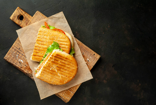 Grilled panini sandwich on wooden chopping board on stone background - Fotó, kép