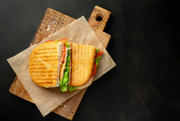 Grilovaný paniniový sendvič na dřevěné sekací desce na kamenném pozadí - Fotografie, Obrázek