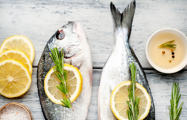 Raw fresh sea bass with lemon slices and rosemary on old wooden background - Photo, image