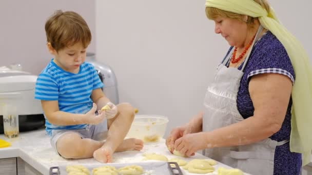 Lähikuva onnellinen hymyili isoäiti ja pojanpoika vaivaamalla tytär yhdessä. vanhuksen ja pienen pojan hidas liike valmistamassa pastaa tai pizzaa yhdessä
. - Materiaali, video