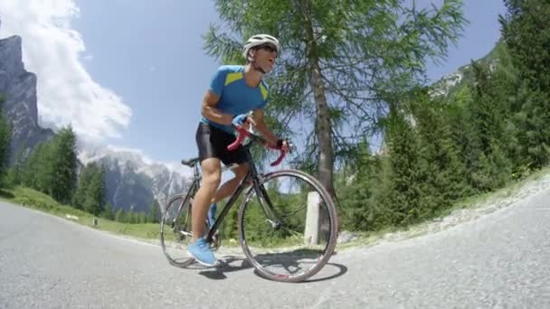 Athletic young male stepping on pedals of his cool road bicycle during intense mountain race. Pro road cyclist training in the sunny mountains. Picturesque bicycle ride in summer nature. - Footage, Video