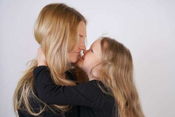 cute kind caucasian blonde mom and daughter posing on white background. a parent and a child experience love and hug. - 写真・画像
