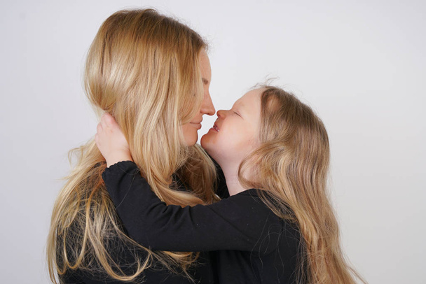 cute kind caucasian blonde mom and daughter posing on white background. a parent and a child experience love and hug. - Foto, imagen