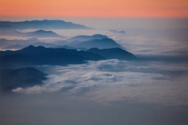 Φωτογραφία από ψηλές βουνοκορφές στην Ανατολή του ηλίου στην Αφρική, κόκκινο και ροδάκινο χρώματα του ουρανού, λευκά σύννεφα τυλίγοντας μαύρη οροσειρά. Ειρηνική σιωπή, μεγάλα ύψη. Αναρρίχηση στο βουνό - Φωτογραφία, εικόνα