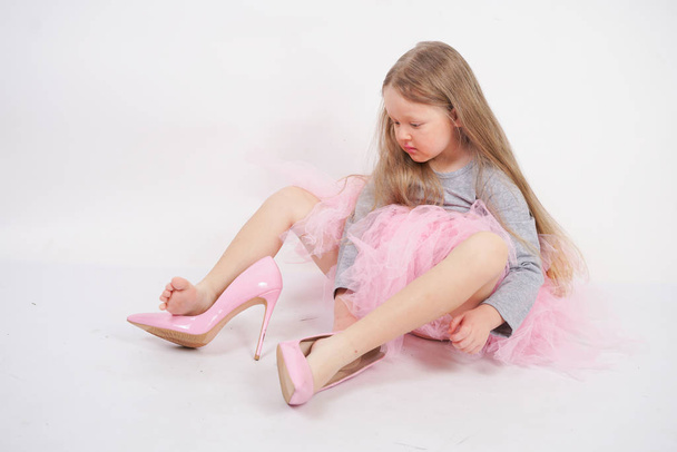 a little caucasian blonde girl sits and puts on her mother's high-heeled shoes. kid wanna to be fashionable and in style. - Φωτογραφία, εικόνα