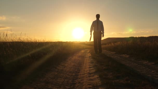 businessman in sunglasses goes down the country road with a briefcase in his hand. The entrepreneur works in a rural area. a farmer inspects the land at sunset. agricultural business concept. - Footage, Video