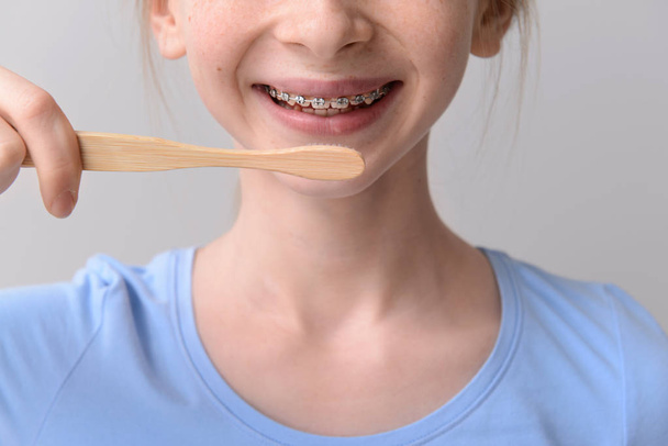 Sonriente adolescente con frenos dentales sosteniendo cepillo de dientes sobre fondo gris
 - Foto, Imagen