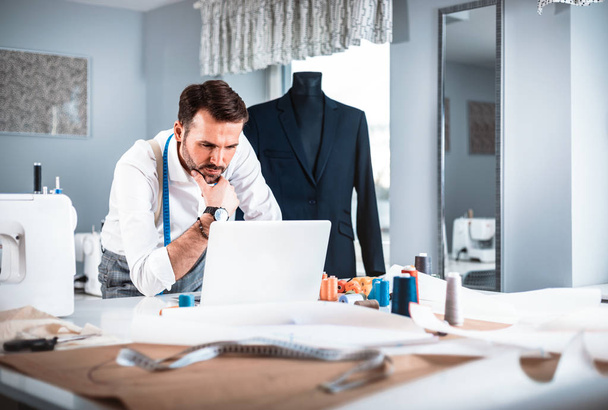 Tailor during work using laptop, modern fashion designer at workshop - Photo, Image