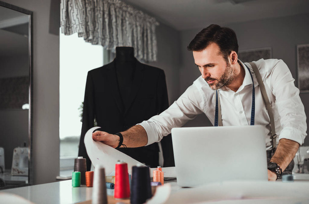 Tailor during work using laptop, modern fashion designer at workshop - Foto, imagen