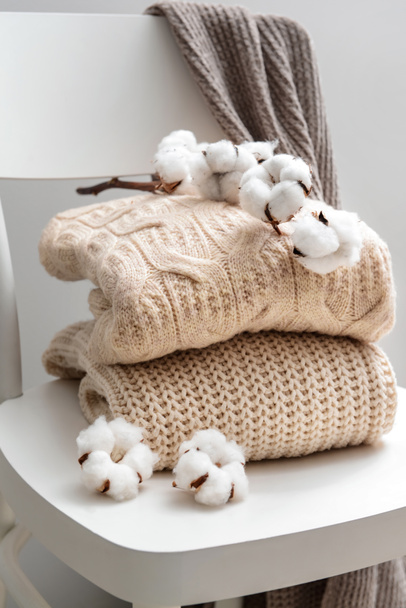 Pletené svetry s bavlněnými květy na bílém křesle - Fotografie, Obrázek