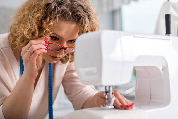 Professional dressmaker woman sews clothes on sewing machine at fashion design workshop - Фото, зображення