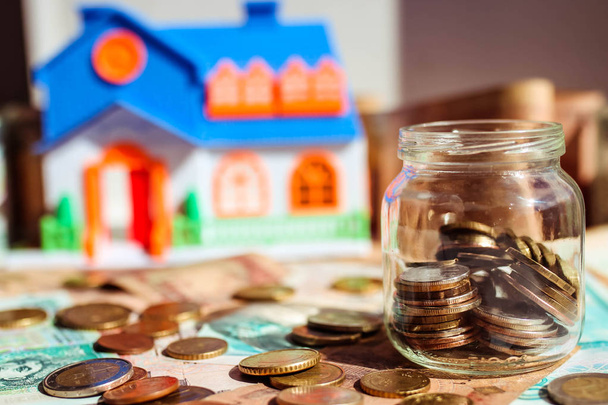 Üvegedénybe érmék pénz területén és a modell a ház az elmosódott háttér. Pénzmegtakarítást, hogy vegyél egy házat koncepció. - Fotó, kép