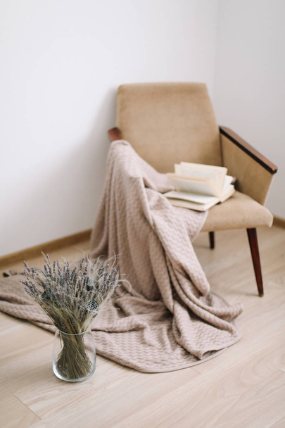 Cozy home decor. armchair with a blanket and a book, a vase with a bouquet of lavender. Modern home interior design. - 写真・画像