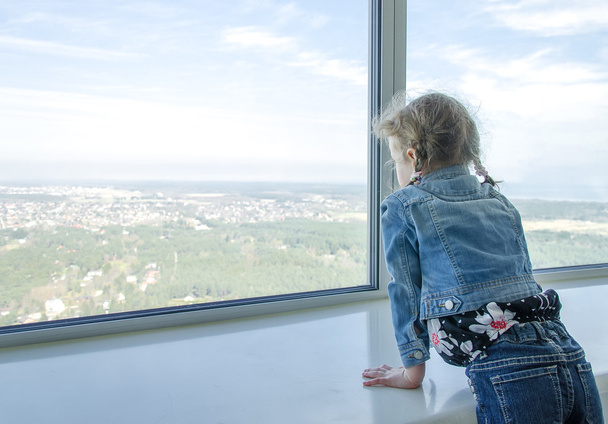 Little girl looking through the window at skyscraper - Foto, Imagen