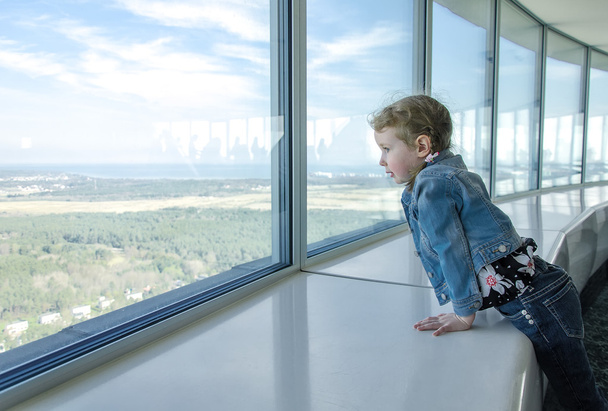 Маленькая девочка смотрит в окно на небоскреб
 - Фото, изображение