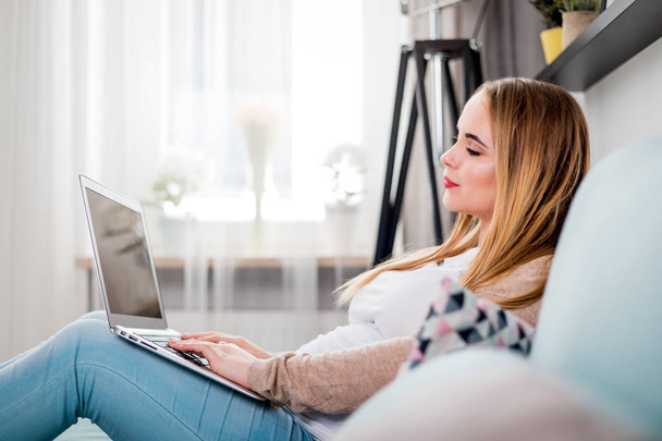 Young pregnant woman using laptop sitting on sofa at home - Foto, Bild