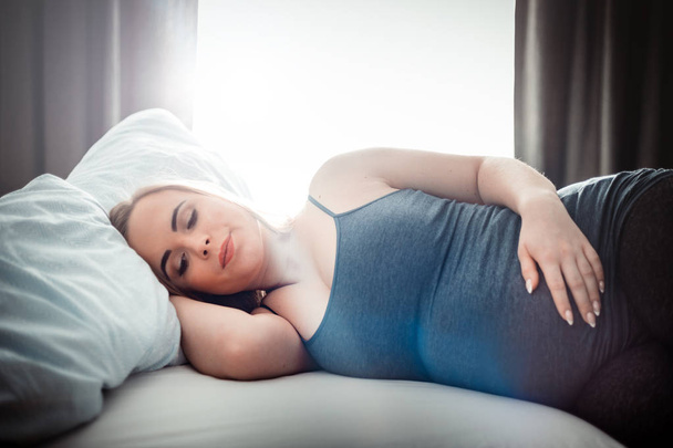 Young pregnant woman sitting on bed and touching her belly, child expectation concept - Foto, Imagen