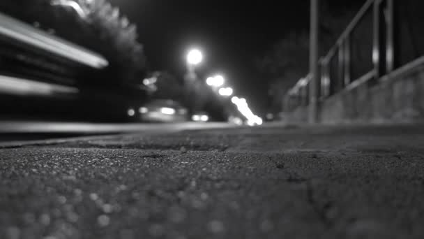 Kaupungin jalkakäytävä valaistu auton ajovalot ajavat ohi yöllä. Musta ja valkoinen valikoiva painopiste
. - Materiaali, video