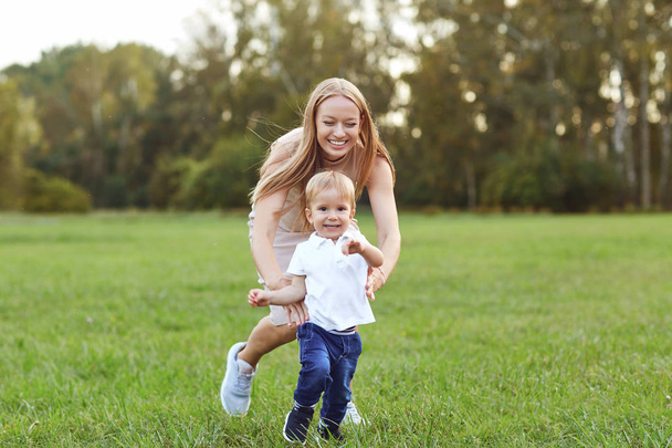 Laughing woman with little boy on green lawn - Фото, изображение