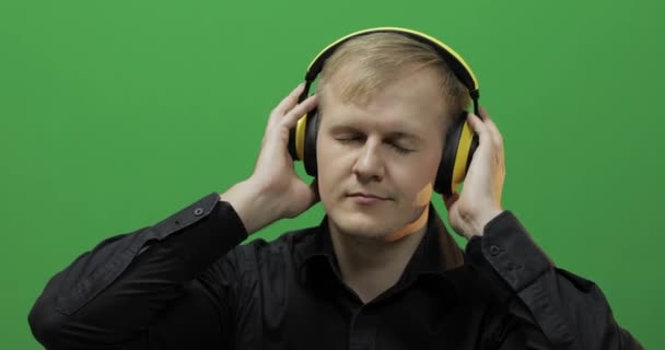 Guy hört Musik mit kabellosen gelben Kopfhörern und tanzt. Grüner Bildschirm - Filmmaterial, Video