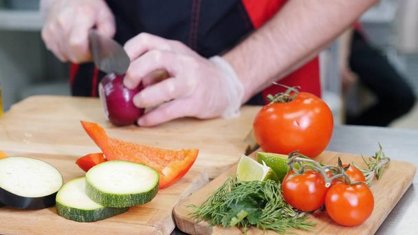 Mutfakta çalışan bir şef. Soğan kesiyor. Ön planda farklı sebzeler - Fotoğraf, Görsel