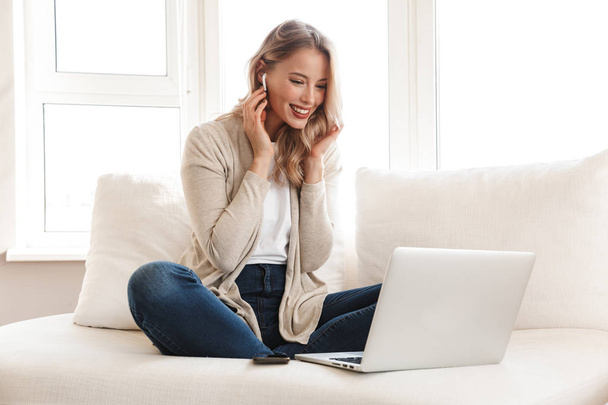 Beautiful blonde woman posing sitting indoors at home using laptop computer. - Photo, Image