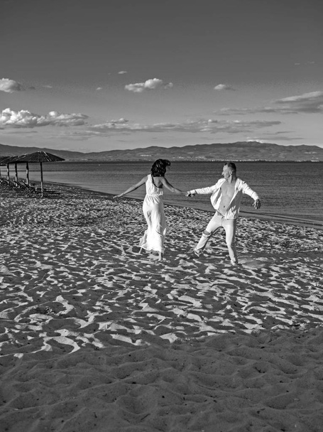 Beautiful happy lovely wedding couple of young paople holding hands standing at water of ocean beach coast and dancing. - Zdjęcie, obraz