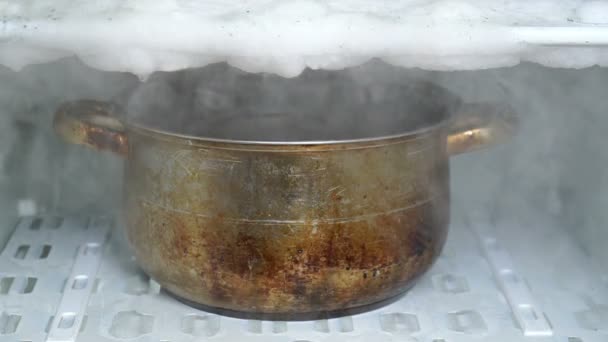 Jégmentesítő hűtőszekrény segítségével nagy konyha fazék tele forró vízzel. Régi piszkos fazék főtt gőzölgő víz áll a hűtőszekrény polcra - Felvétel, videó