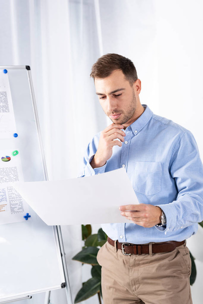 pensive businessman looking at blank paper while standing near white board in office  - Photo, Image