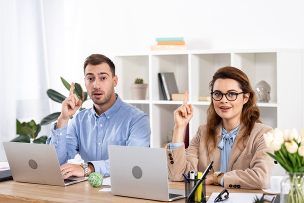 surprised woman sitting with coworker and gesturing in office  - Foto, Imagem