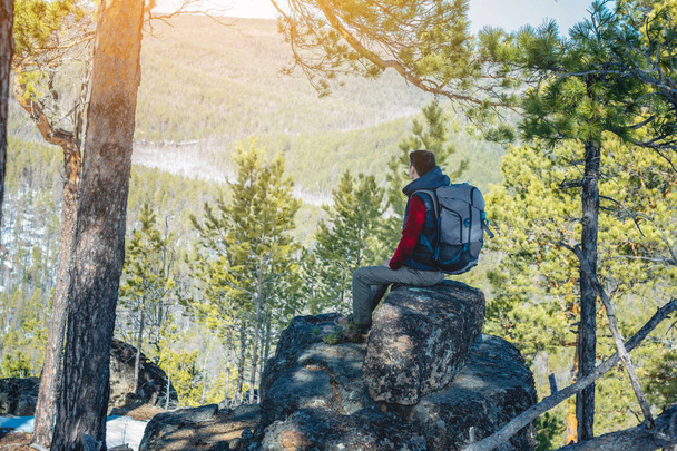 Man wandelaar met een grote rugzak zittend op een rots klif en kijken naar de uitgestrekte groene vallei. Vrijheid in reizen - Foto, afbeelding