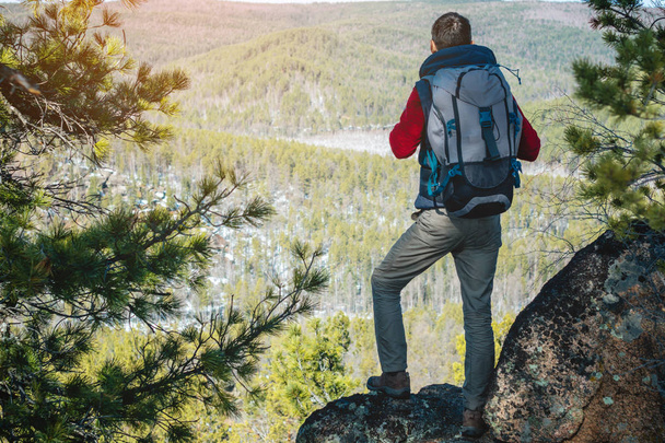 Man toerist met een grote rugzak staat op een rotswand en kijkt naar de uitgestrekte groene vallei. Vrijheid in reizen - Foto, afbeelding