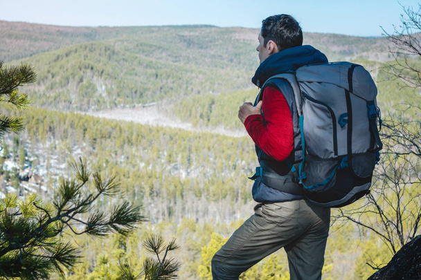 大きなバックパックを持つ男性観光客は、岩の崖の上に立って、広大な緑の谷を見ています。旅行の自由 - 写真・画像