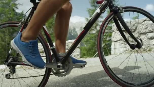 Athletic young male stepping on pedals of his cool road bicycle during intense mountain race. Pro road cyclist training in the sunny mountains. Picturesque bicycle ride in summer nature. Slow motion footage - Footage, Video