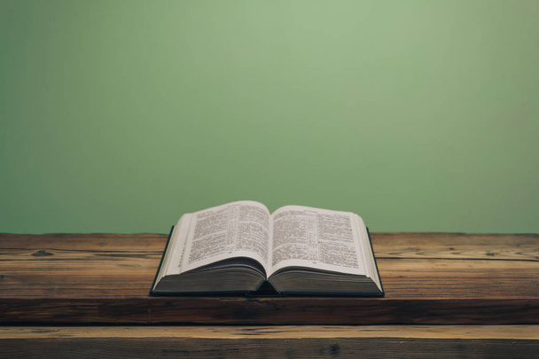 Apri la Sacra Bibbia su un vecchio tavolo in legno di quercia. Fondo muro verde. - Foto, immagini